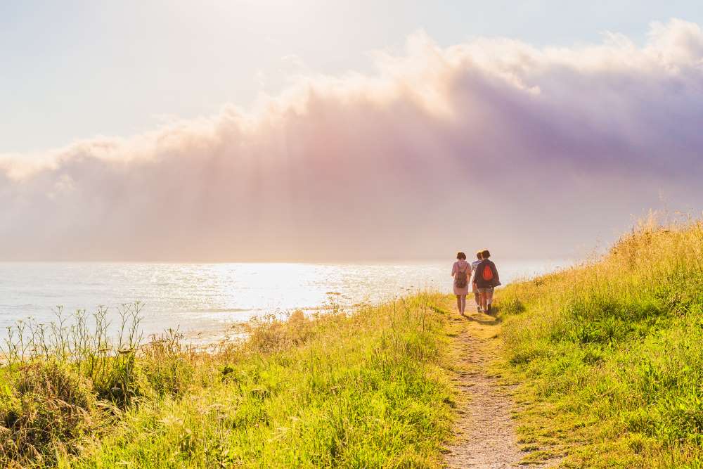 a picture of 2 pilgrims walking along the sea on a path