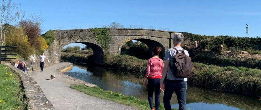 a picture of 2 pilgrims walking along the river. There is a bridge across the river on the Camino
