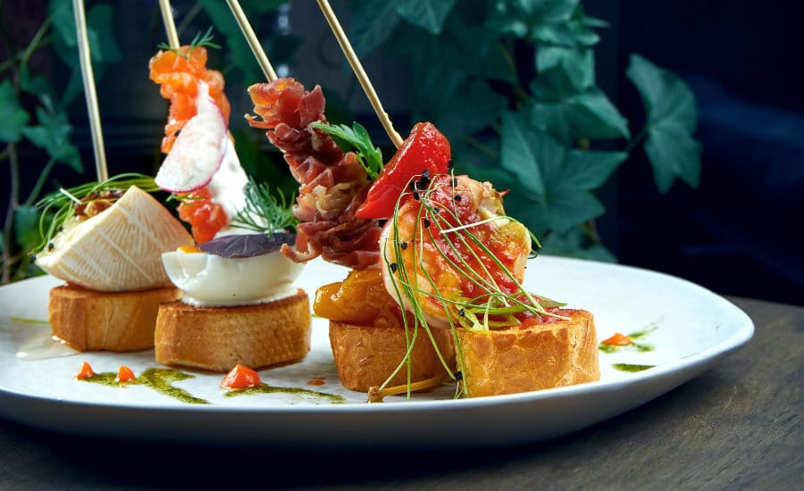 Classic Spanish Antipasto - Pintxos or Tapas with Shrimp, Camembert, Salmon and Jamon in a White Plate. Selective Focus
