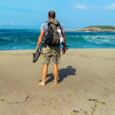 Pilgrim standing on beach with trekking shoes and backpack