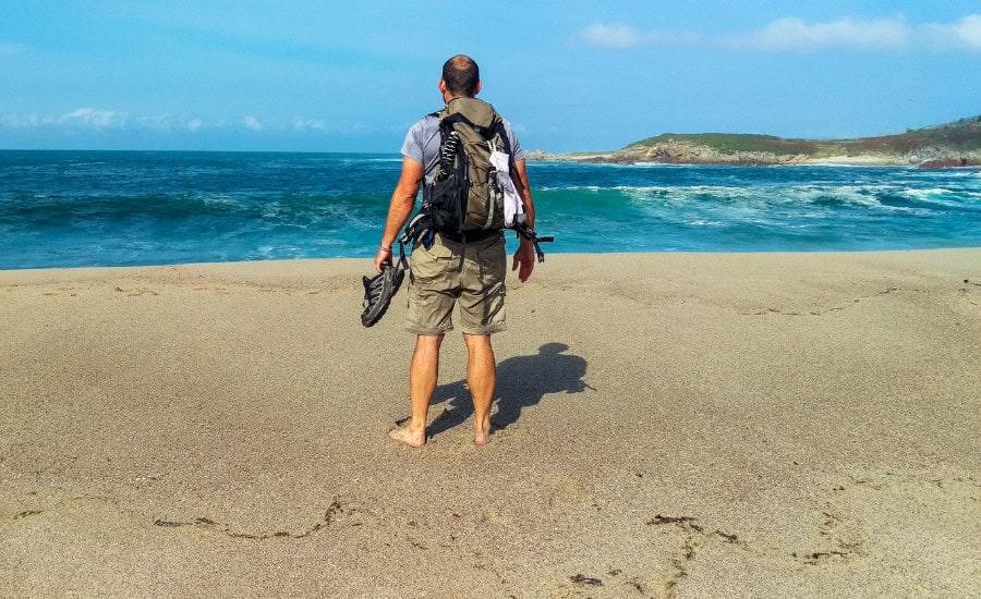 Pilgrim standing on beach with trekking shoes and backpack