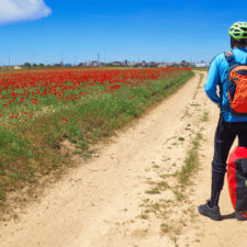 Cyclist pilgrim posing by red flower path on the Camino frances