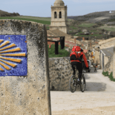 2 cyclists cycling past yellow arrow sign camino de santiago