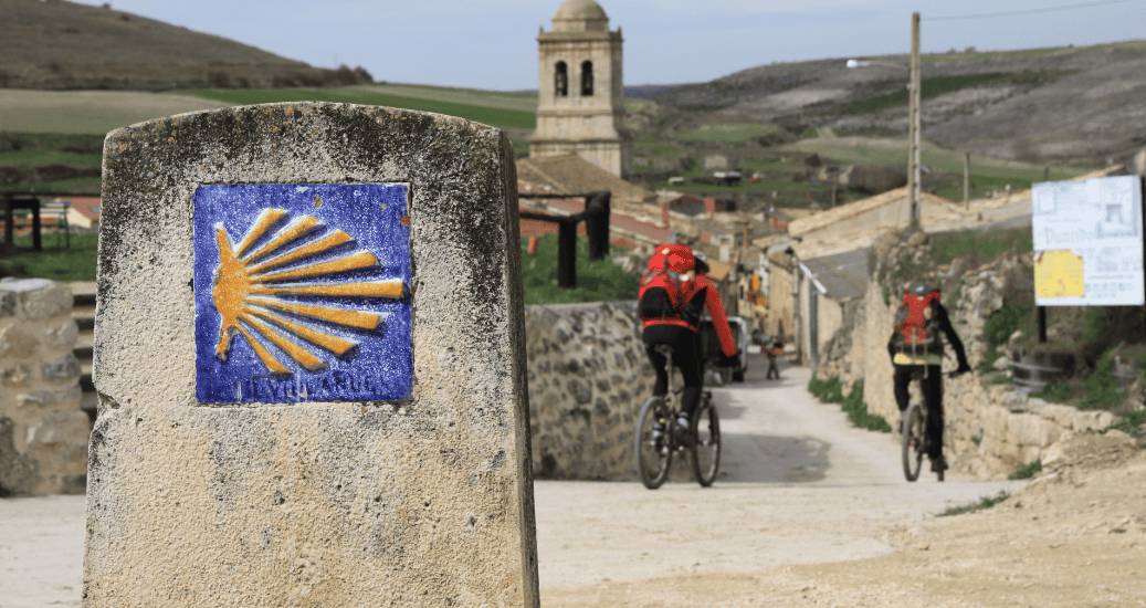 2 cyclists cycling past yellow arrow sign camino de santiago