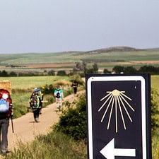 Pilgrims walking on camino path with yellow arrow