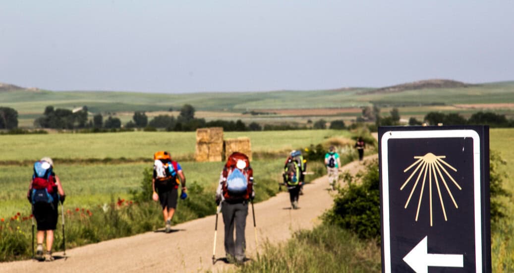 Pilgrims walking on camino path with yellow arrow