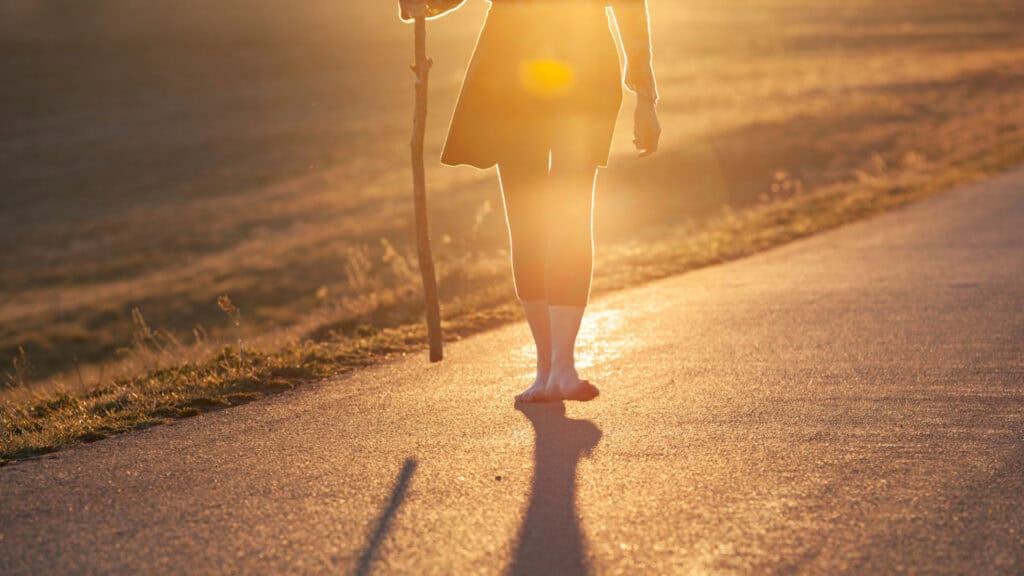 Woman pilgrim walking the Camino with the sun shining behind her